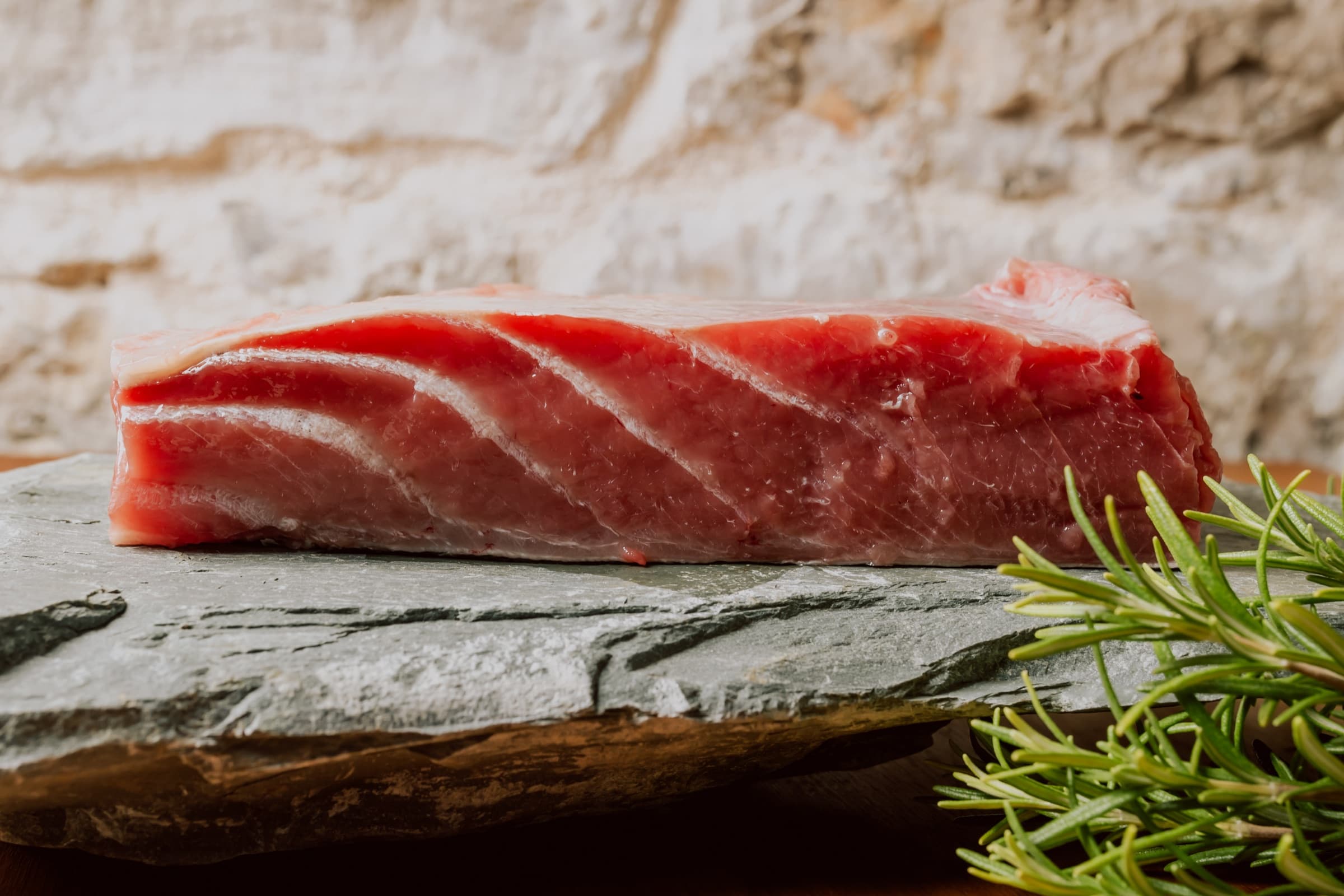 A fresh tuna filet on a slate board beside a sprig of rosemary