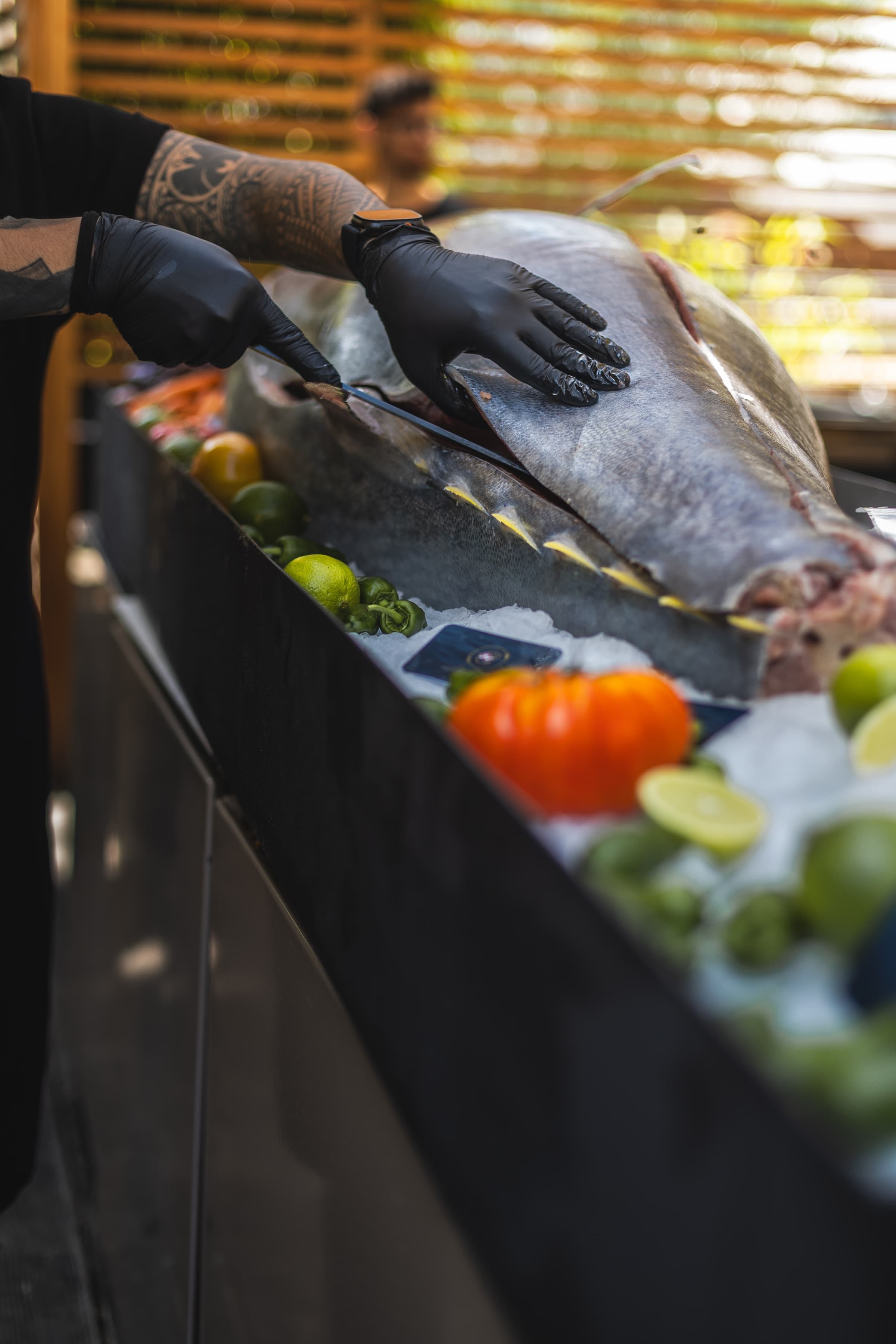 A tuna cutting show presenter in black gloves cutting a whole bluefin tuna on ice